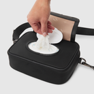 hand pulling baby wipes from wipes dispenser of crossbody baby bag
